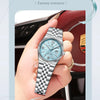 A close-up shot of a silver stainless steel quartz wristwatch with a light blue dial and luminous hands worn on a person's ha