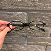 Une paire de lunettes ovales noires tient contre un mur de briques grises.