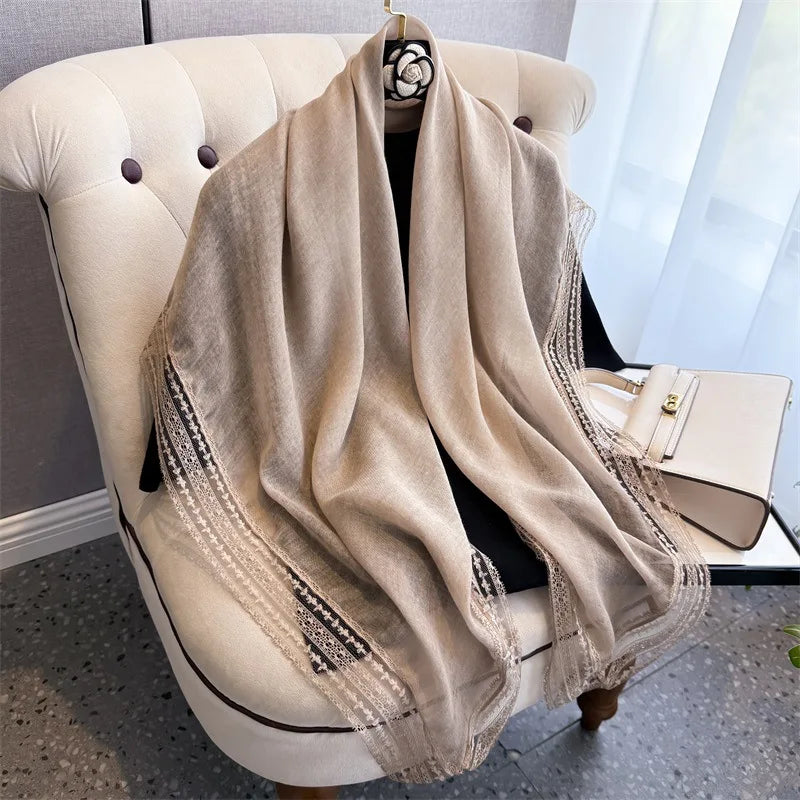 A beige shawl with intricate lace trim draped over a cream upholstered armchair.