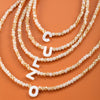 A collection of layered pearl necklaces featuring individual initial letters like C, U, L, and O.