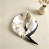 A white silk scarf with a black print and a pearl detail is displayed on a beige fabric.