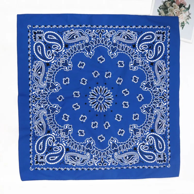 A vibrant blue bandana scarf featuring intricate white paisley and floral patterns.