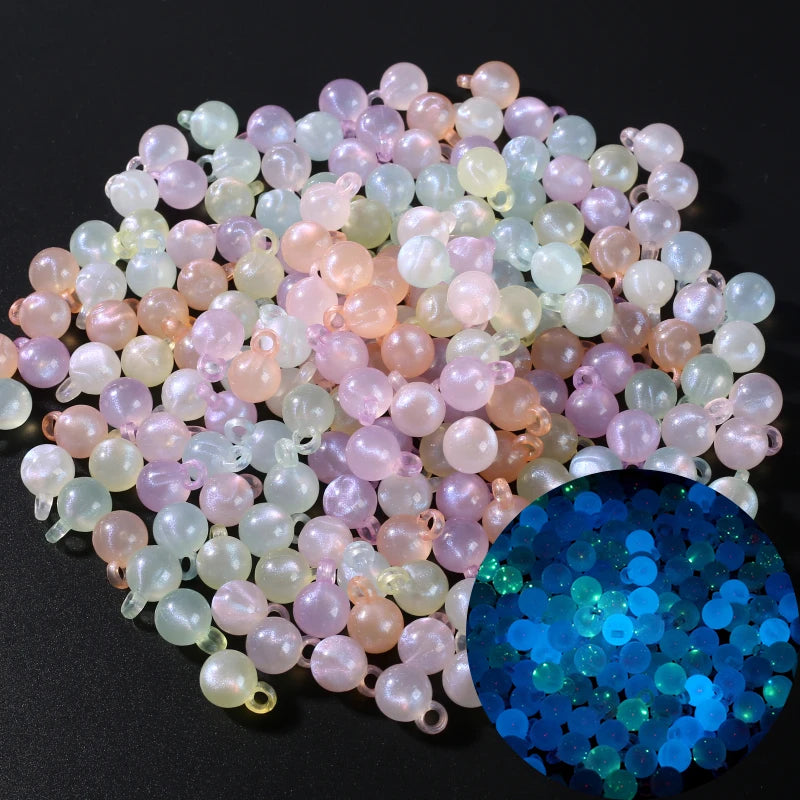 A pile of luminous glow-in-the-dark acrylic beads in shades of pink, peach, and pale green scattered on a dark surface.