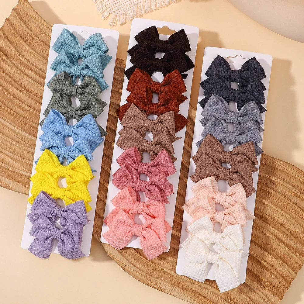 A collection of handmade ribbon bow hair clips in various shades of gray, brown, purple, and yellow displayed on a wooden boa