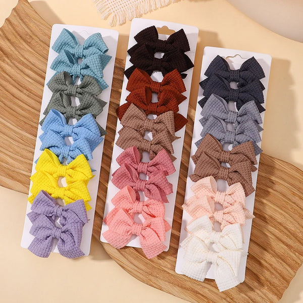 A collection of handmade ribbon bow hair clips in various shades of gray, brown, purple, and yellow displayed on a wooden boa