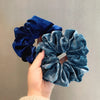 A hand is holding a dark blue velvet heatless hair curling scrunchie with ruffled texture.