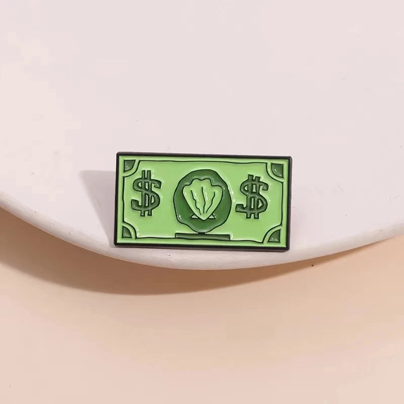 A green enamel dollar banknote brooch featuring an ocean shell charm.