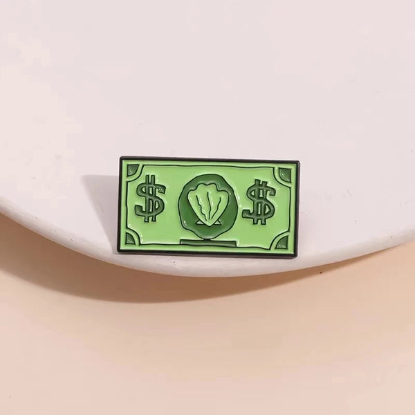 A green enamel dollar banknote brooch featuring an ocean shell charm.