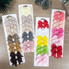 Un set de pinzas para el pelo con lazos de colores sólidos para niños, incluyendo amarillo, rosa, rojo y gris.