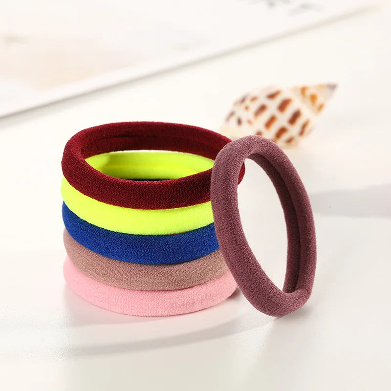 A stack of ten colorful elastic hair ropes in shades of red, green, yellow, blue, purple, and pink resting on a white surface