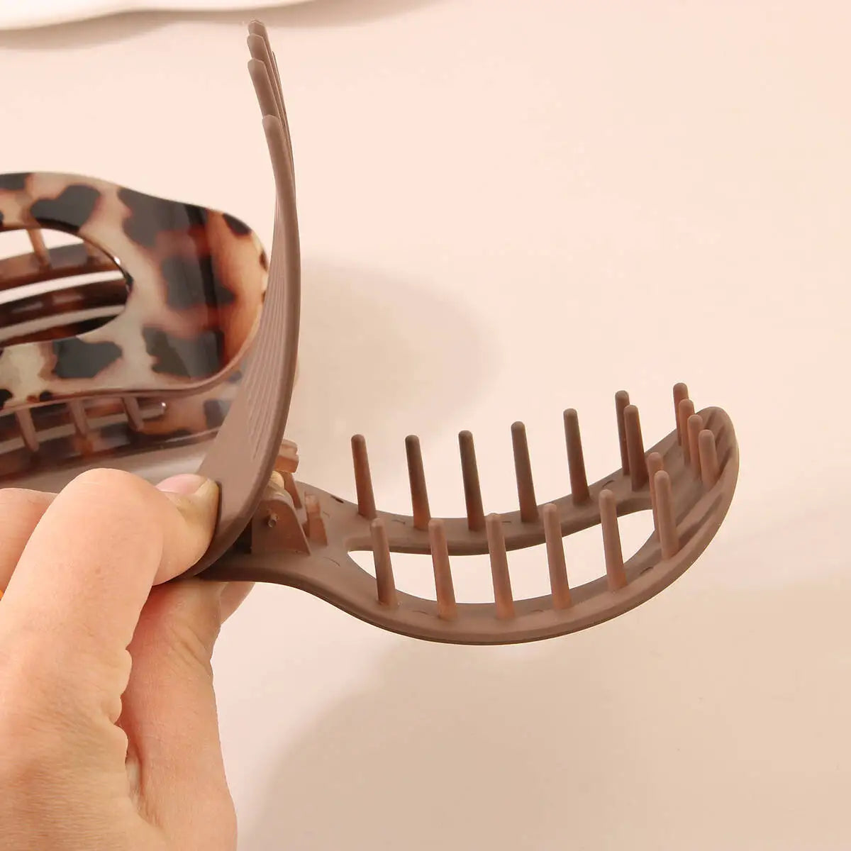 Eine Hand hält eine braune, ovale Haarklemme mit Zinken und demonstriert das Produkt.