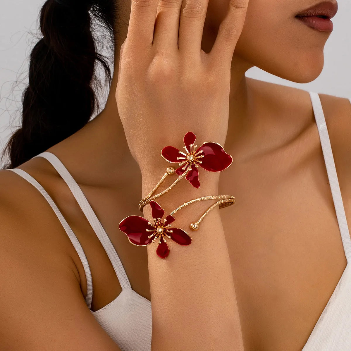 A close-up of a woman's wrist wearing an elegant floral open cuff armlet jewelry with red and gold accents.
