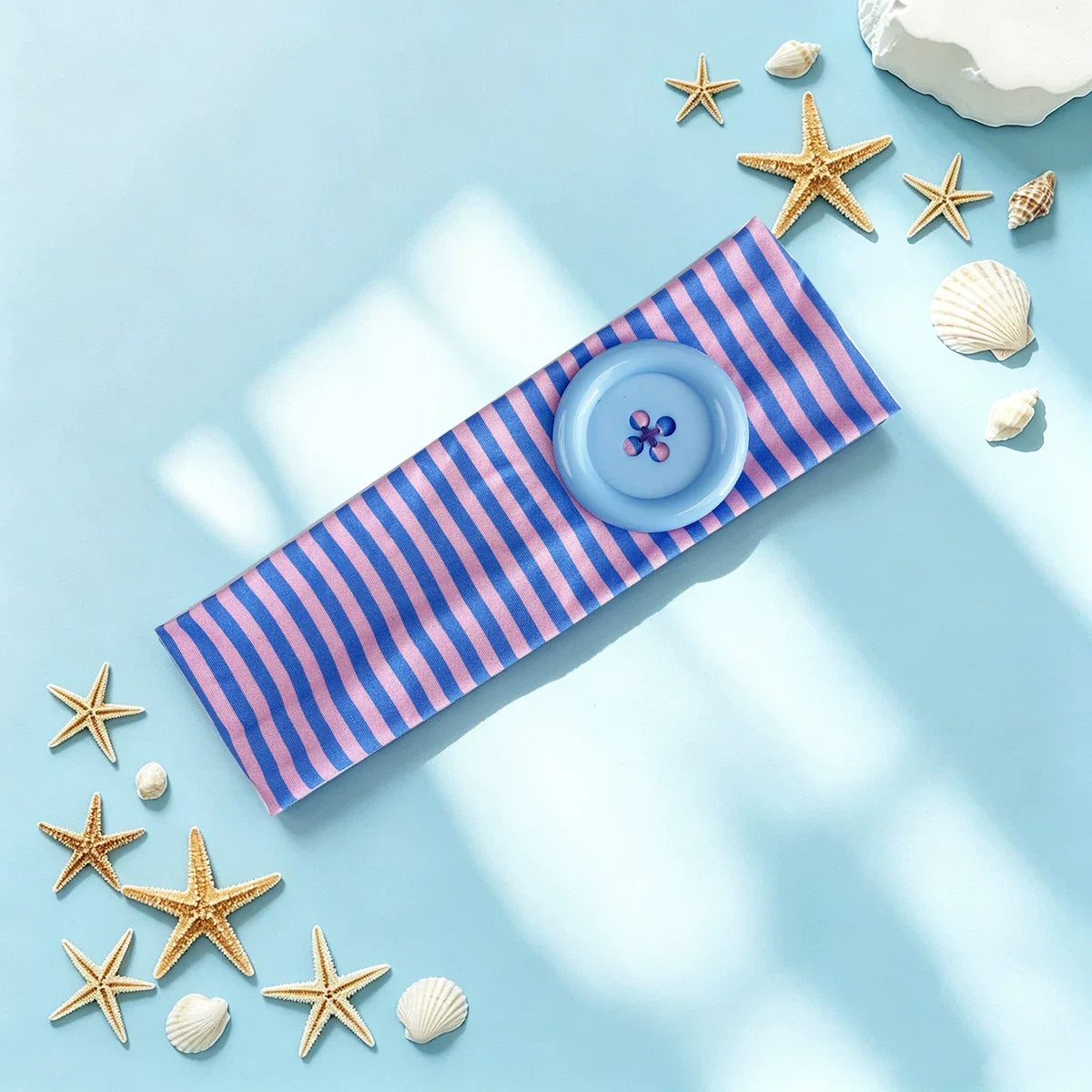Bande de tissu rayée bleu et rose avec motif de fleur violette posée sur une surface bleu clair entourée d'étoiles de mer et 
