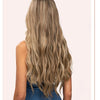 Una mujer muestra extensiones de cabello rubio largo y ondulado con suaves ondas.