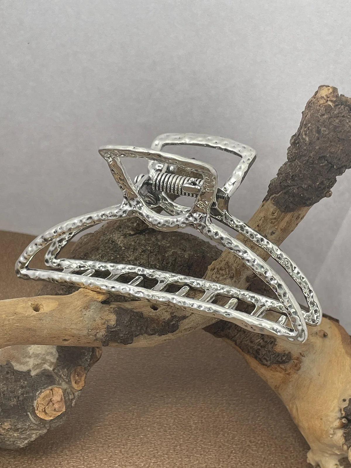 Silver metal hair claw clips with a turquoise bead design resting on a piece of driftwood.