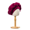 A deep magenta braided turban cap displayed on a wooden mannequin stand.