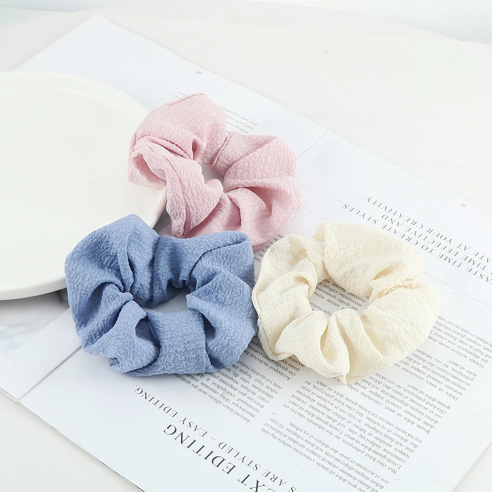 Three knitted hair scrunchie headbands in pink, blue, and cream colors displayed on a white background.