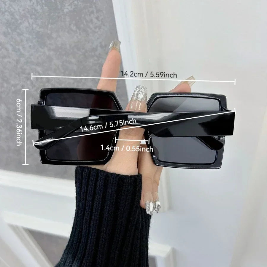 Black square sunglasses being held by a hand, showing dimensions.
