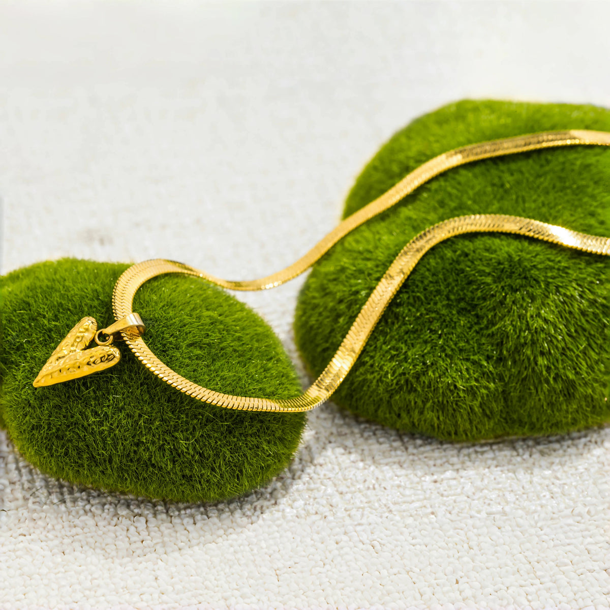 Goldene Schlangenkette mit Herzanhänger auf moosgrüner Stoff