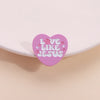Broche émaillée en forme de cœur rose avec le texte Love Like Jesus et des fleurs roses et violettes.