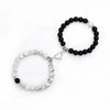 A pair of natural stone heart couple bracelets, one black and one white, displayed against a white background.