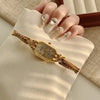 A close-up of an elegant gold quartz fashion wristwatch worn on a hand, set against a light beige fabric background.