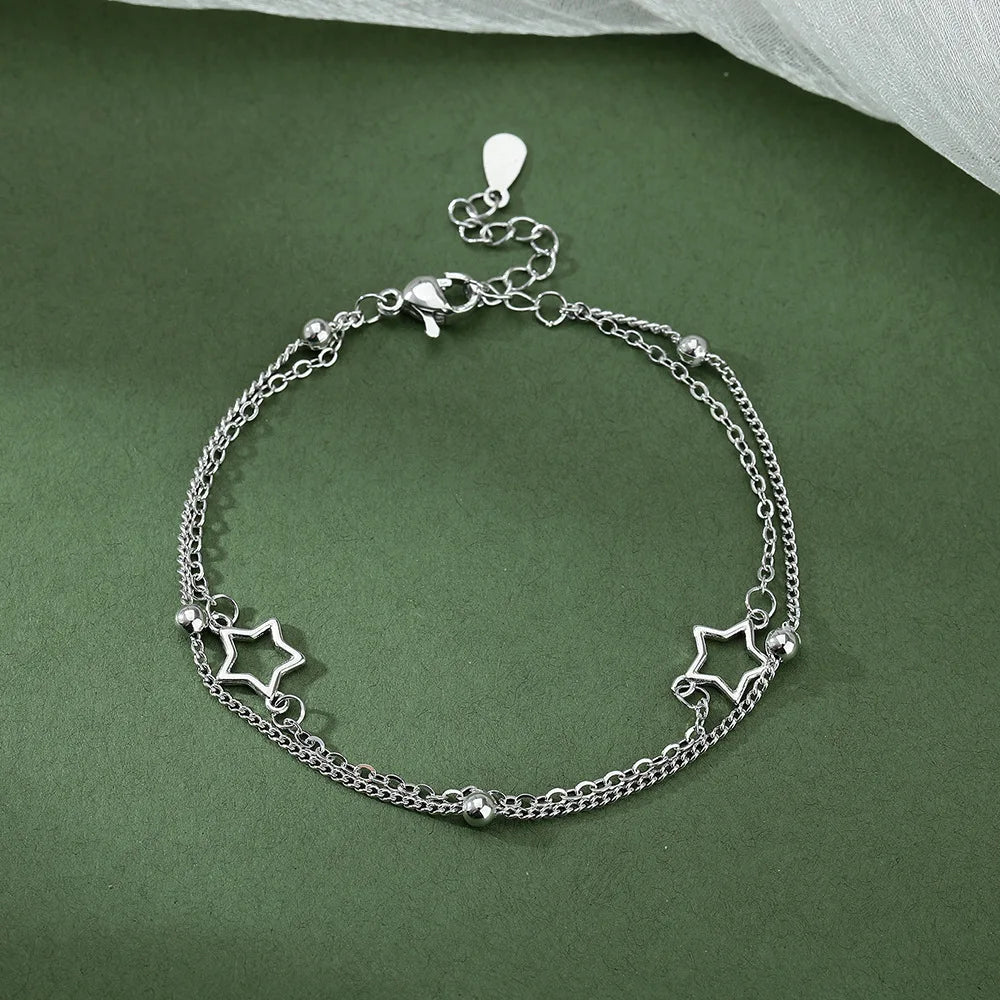 Sterling silver double heart charm bracelet with a chain and star charms displayed on a green background