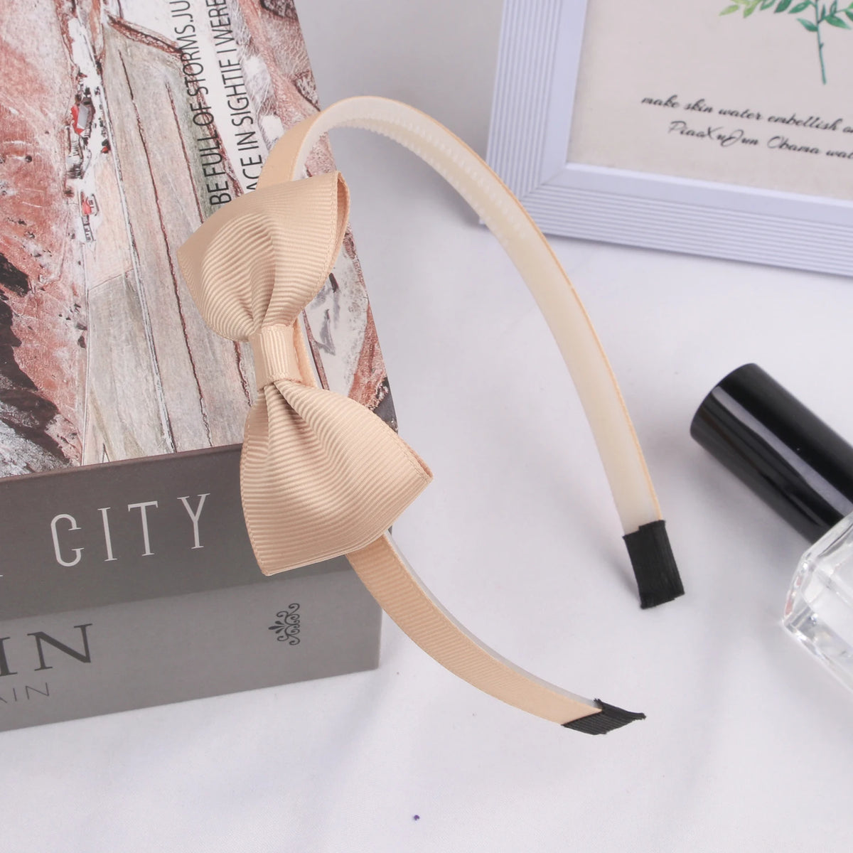 A light beige grosgrain ribbon hair bow is displayed next to a black cosmetic product and a box.