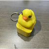 A yellow fidget frog keychain with a black eye and orange beak resting in its clear plastic container.
