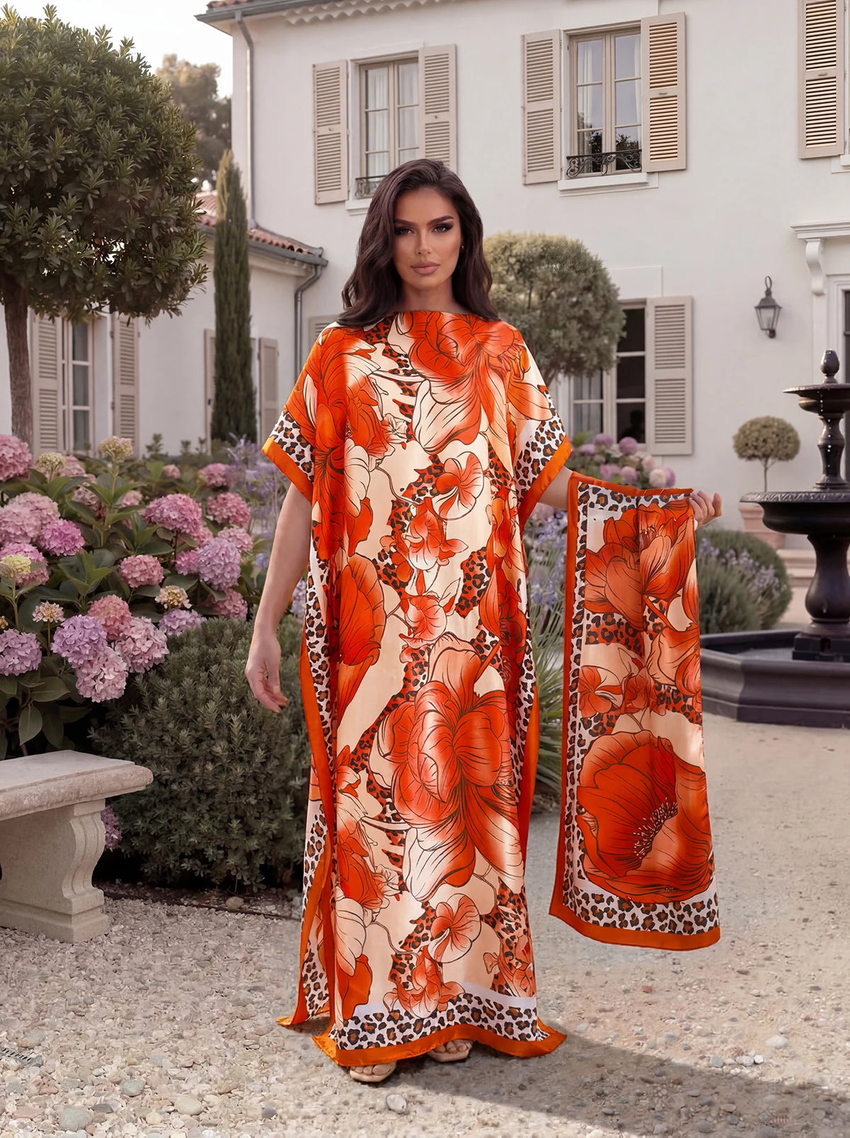 An orange tropical floral leopard print abaya scarf worn by a model outdoors near a white building.