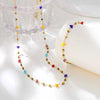 A delicate gold chain necklace featuring irregular colored gemstone beads, displayed next to a clear glass bowl.