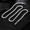 A silver rope charm necklace with a clasp is displayed on a black leather surface.