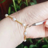 A hand is wearing a delicate gold-toned necklace with small white pearl beads and a silver tool attached.