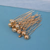 A cluster of 18 gold-toned faux pearl hair pins arranged on a light blue surface.