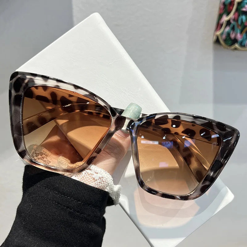 Pair of brown leopard print cat eye sunglasses resting on a white surface.