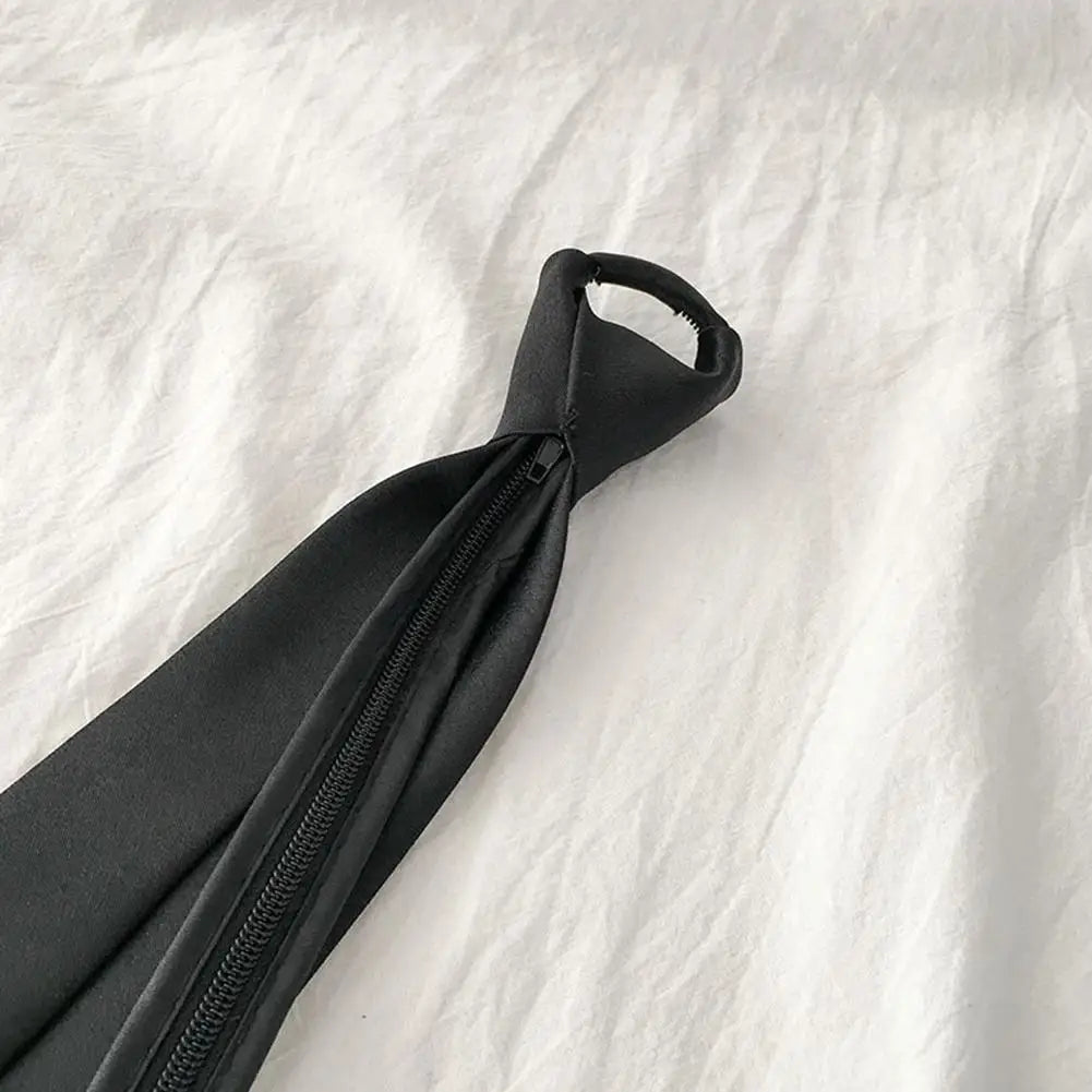 A black clip-on tie is shown lying on a white fabric background.