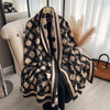 A black and beige patterned cashmere scarf draped over a hanger in a bright room.