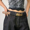 A close-up of a woman wearing dark denim pants and a gray top, featuring a brown belt with bronze rivets.