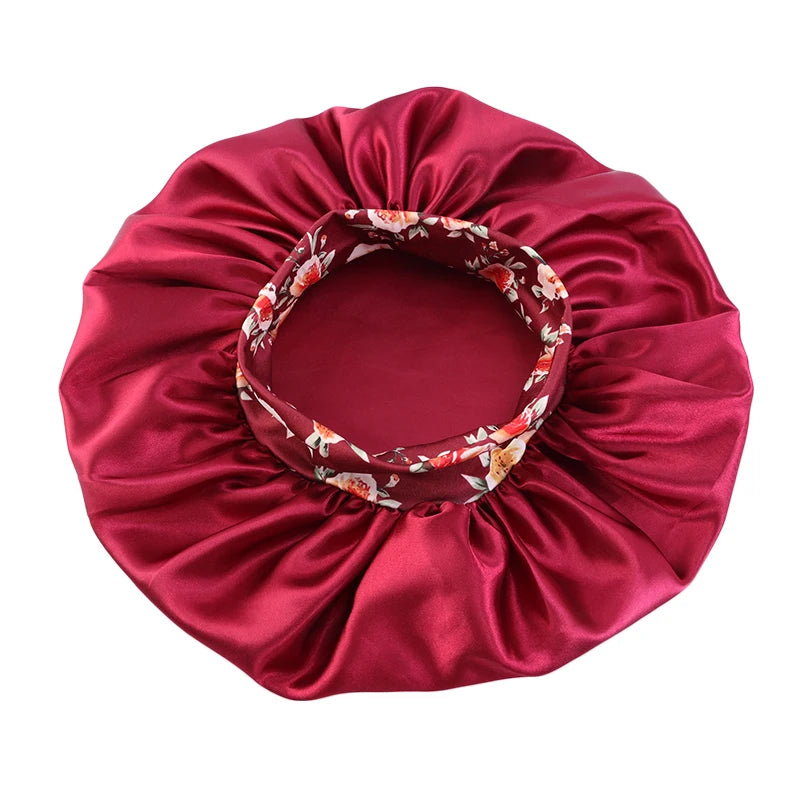 A deep red satin sleep bonnet with a floral pattern and an elastic band.