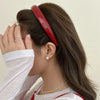 A woman shows her face with her hand while wearing a red PU leather fashion headband.