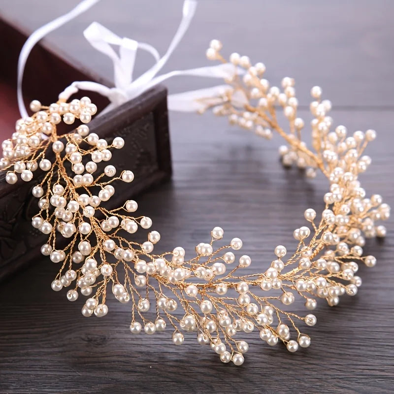A delicate gold pearl hair vine headband with white ribbon, displayed on dark wood.