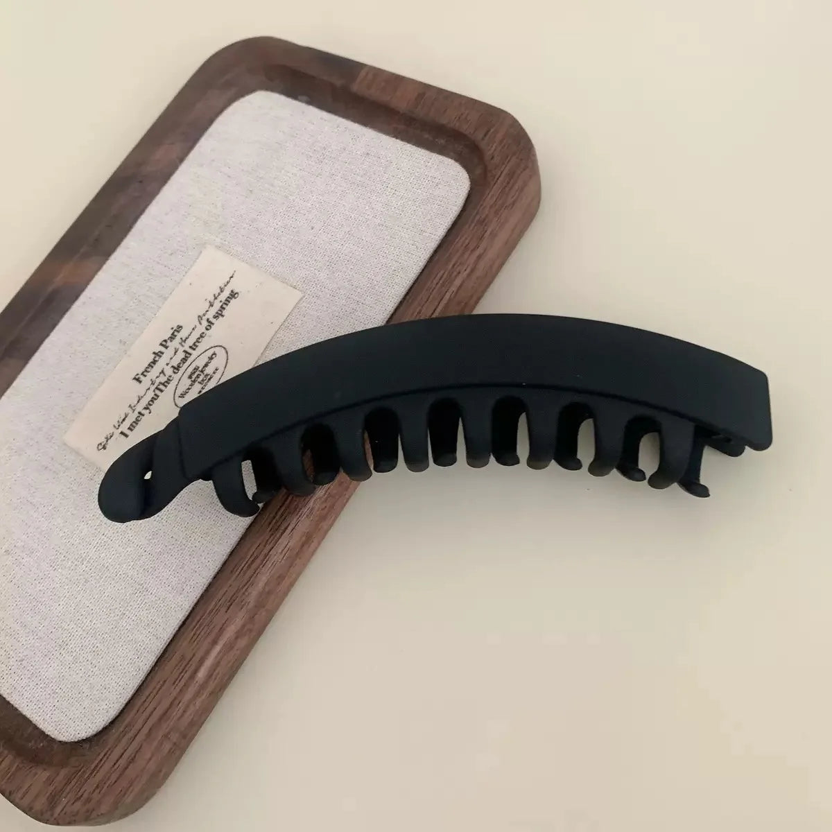 A black set of large banana hair clips resting on a wooden tray with a white cloth.