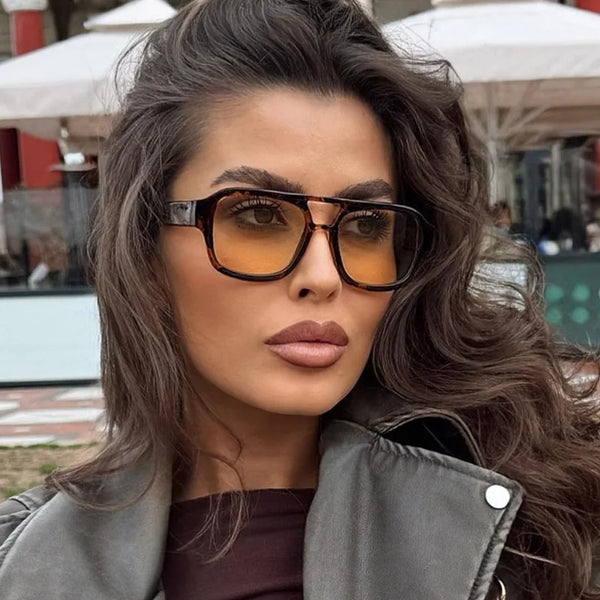 A woman models vintage square sunglasses with a double bridge and dark brown hair outdoors.