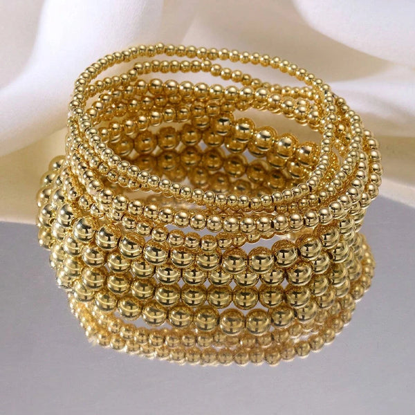 A stack of gold-colored minimalist round beaded bracelets for women