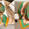 A silk scarf with a floral print featuring green, orange, and gold tones draped on a beige fabric.