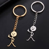 A pair of gold and silver keychain charms shaped like stick figures, one making a middle finger gesture.