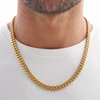 A close-up of a men's gold Cuban link chain necklace worn around the neck against a white shirt.