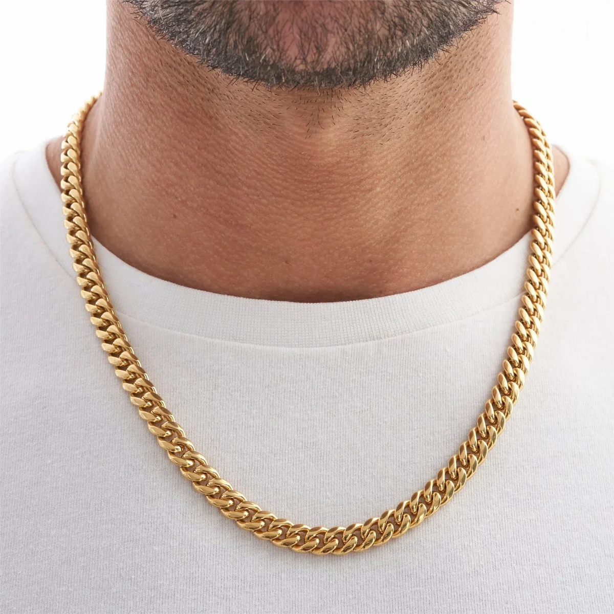 A close-up of a men's gold Cuban link chain necklace worn around the neck against a white shirt.