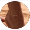 Layered gold and silver plated anklets worn on a person's ankle against a sandy background.