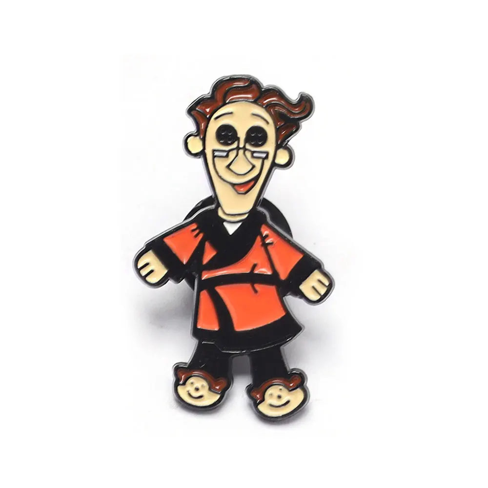 Une épingle émail avec un personnage souriant et caricatural aux cheveux brun-roux et une tenue orange.